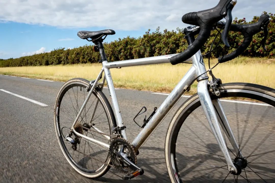 Vélo de route gris sur une route de campagne, ciel bleu avec quelques nuages.