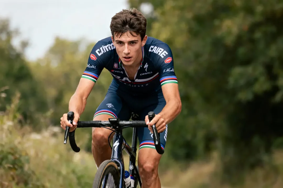 Cycliste en tenue bleue roule en extérieur sur route bordée d'arbres.