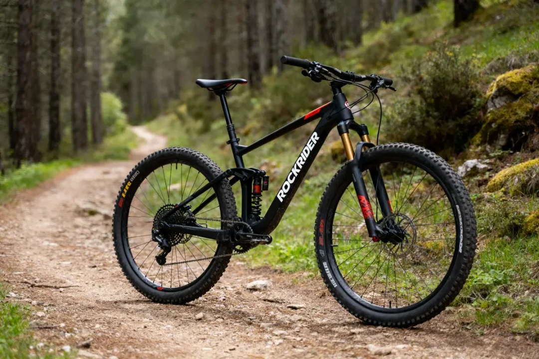 VTT noir Rockrider sur sentier forestier en terre, entouré d'arbres et de verdure.