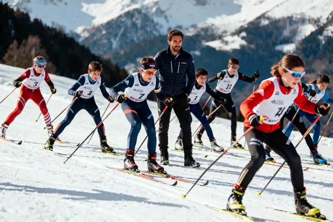 Des enfants pratiquent le ski de fond en groupe, encadrés par un moniteur, sur une piste enneigée.