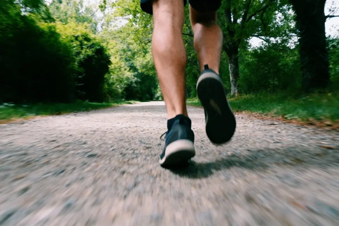 Personne courant sur un chemin de gravier entouré d'arbres verts. Vue rapprochée des jambes et chaussures.