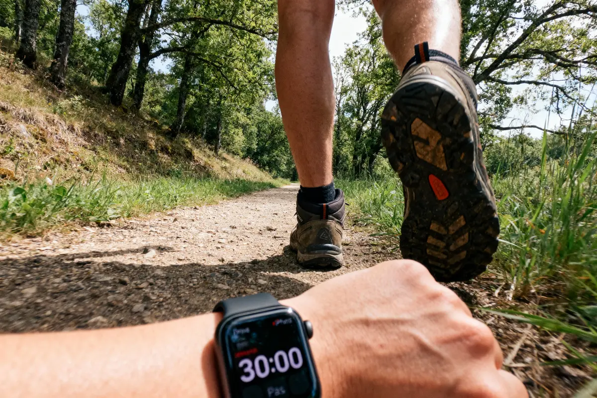 Un randonneur sur un sentier forestier, montre avec montre affichant 30:00. Chaussures de marche visibles.