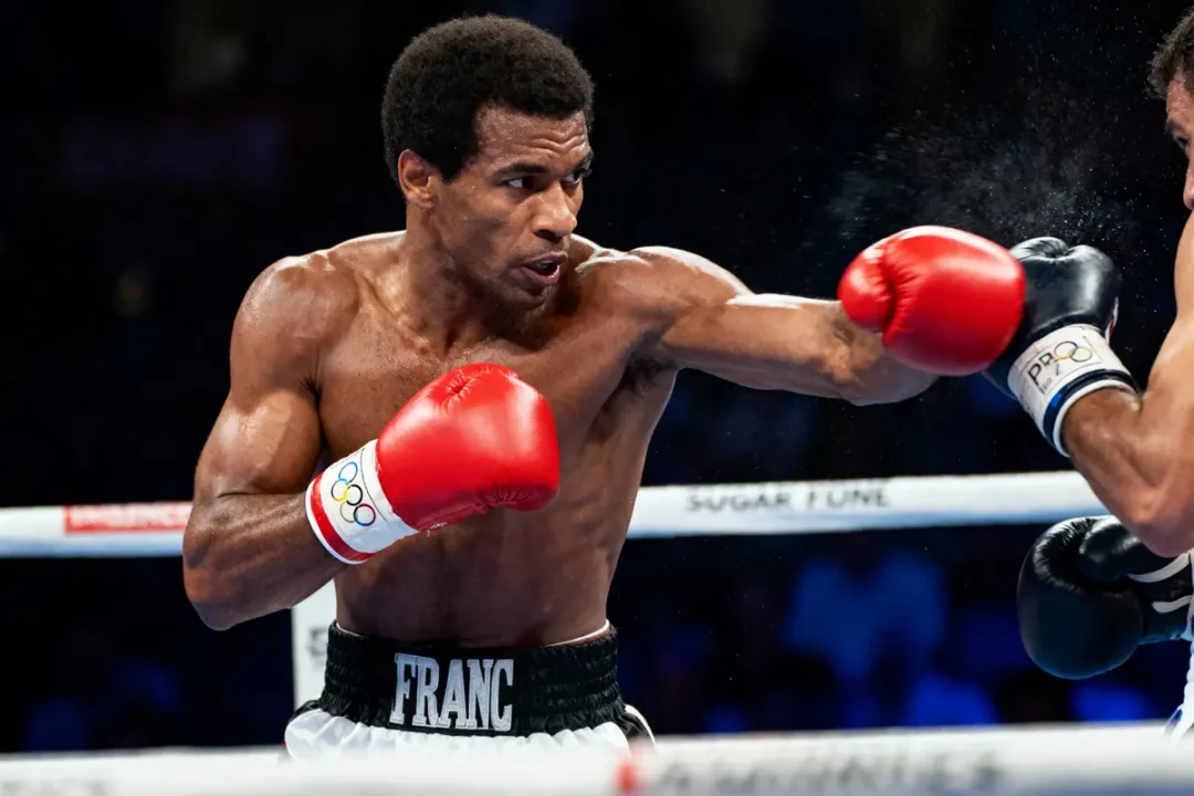 Boxeur en action, frappant avec des gants rouges, dans un ring de boxe. Deux combattants s'affrontent intensément.