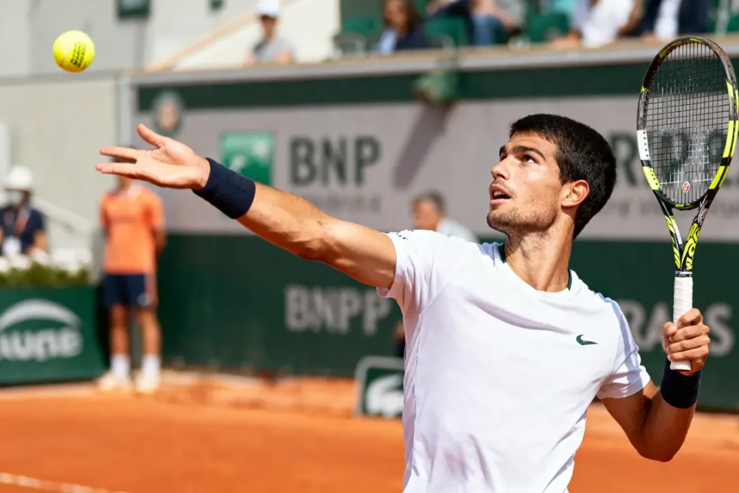 Un joueur de tennis prépare un service sur un court en terre battue, balle et raquette en main.