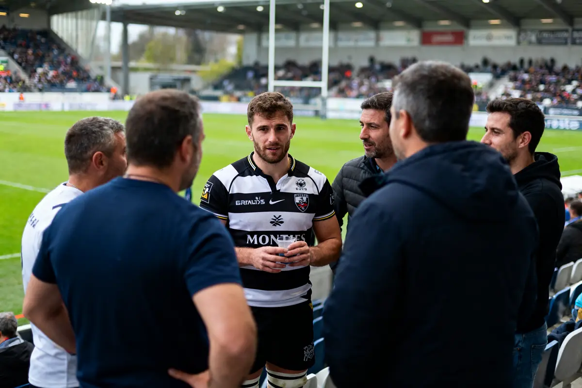 Joueur de rugby discutant avec plusieurs hommes près du terrain lors d'un match.