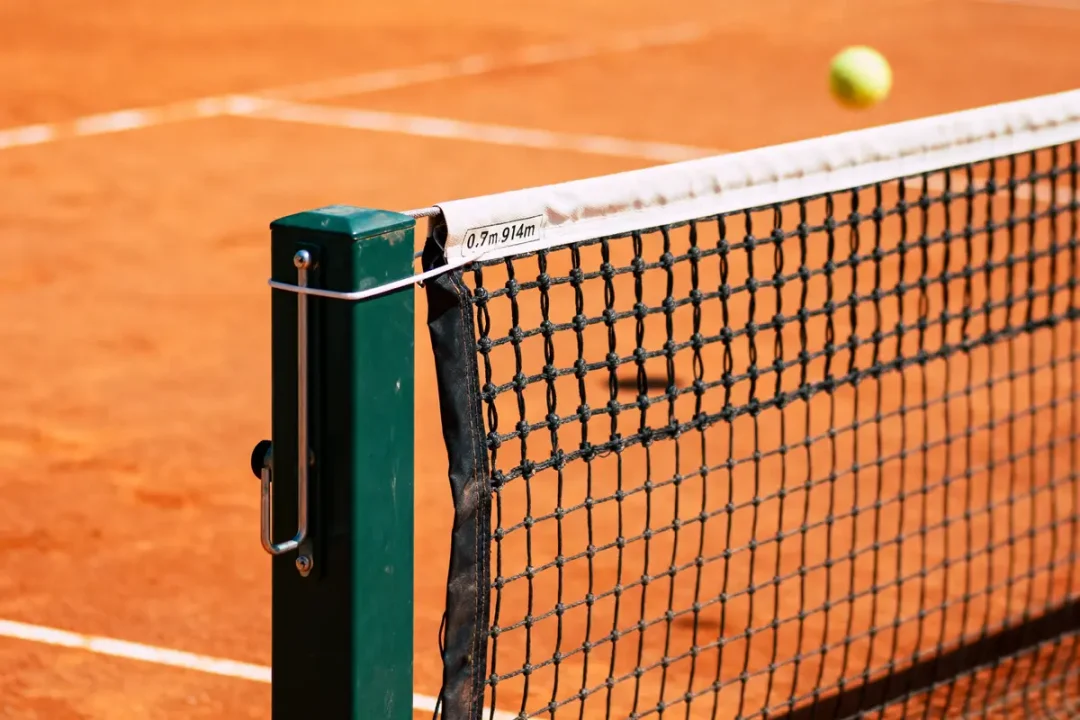 Filet de tennis sur terre battue avec balle en arrière-plan.