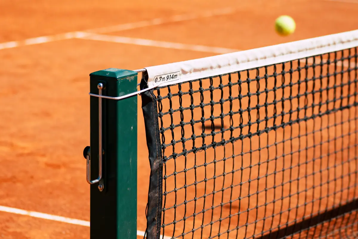 Filet de tennis sur terre battue avec balle en arrière-plan.