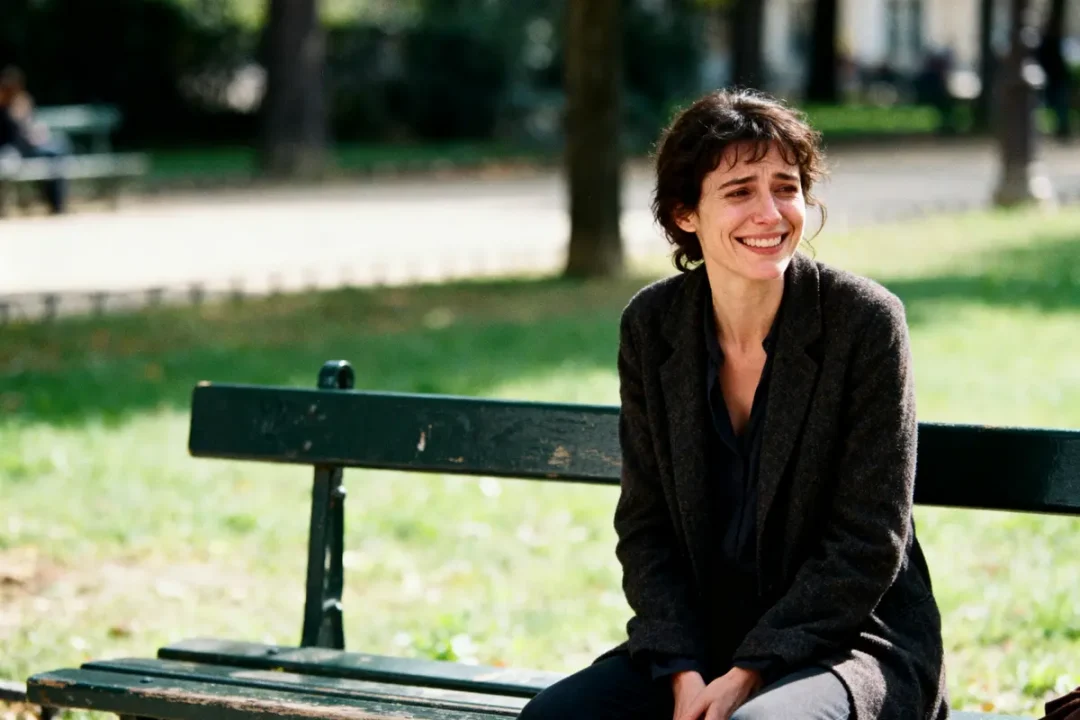 Une femme souriante est assise sur un banc dans un parc ensoleillé.