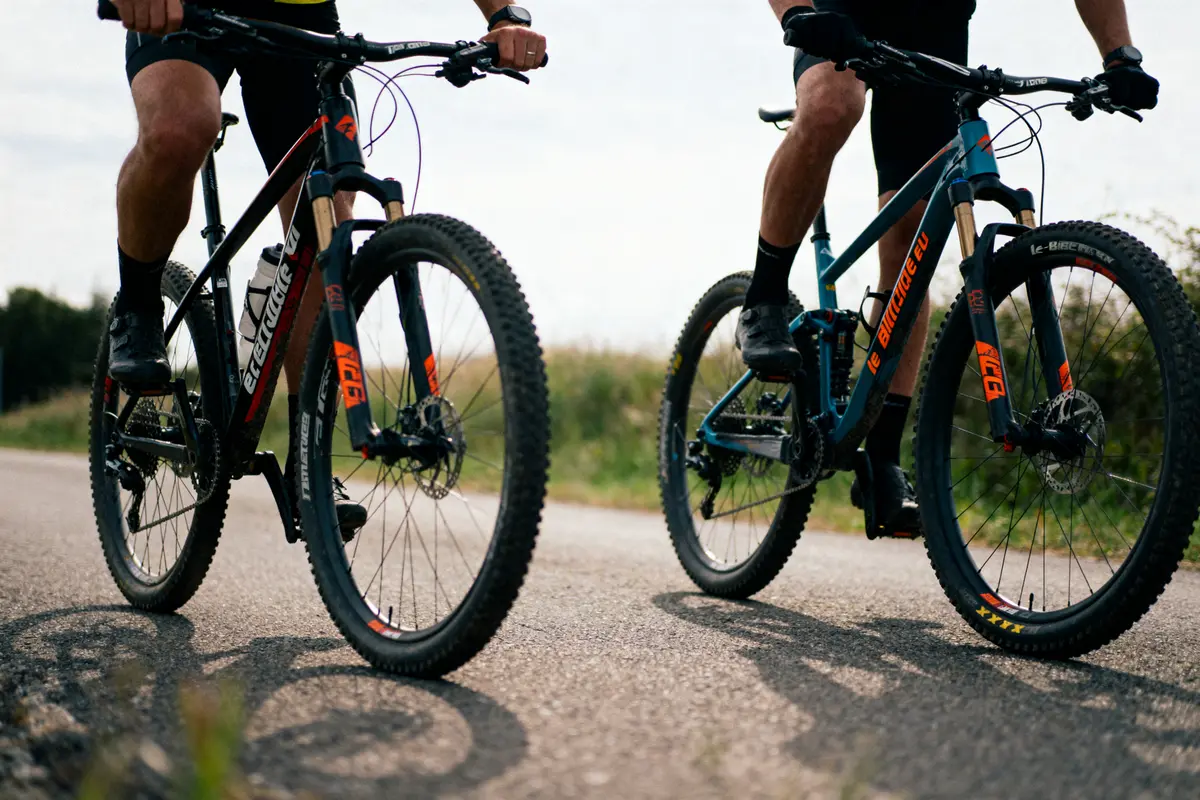 Deux personnes font du vélo de montagne sur une route, portant des équipements de cyclisme.