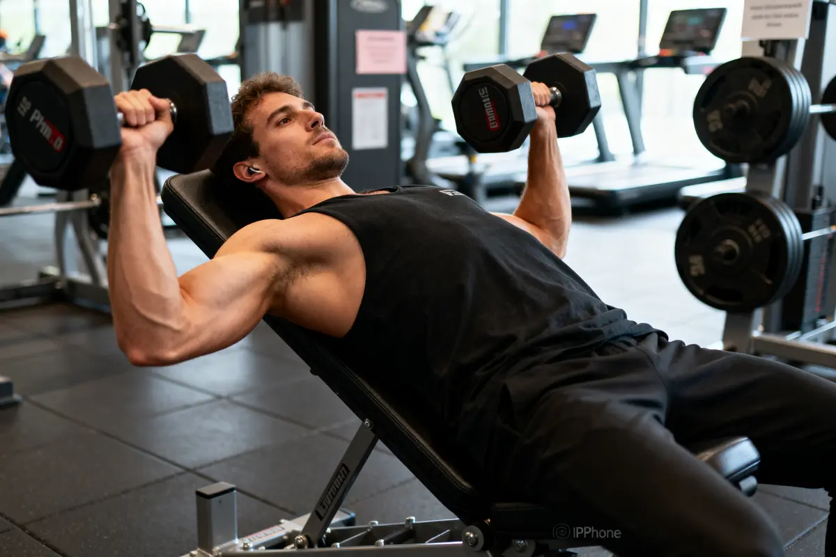 Homme faisant du développé couché avec haltères dans une salle de sport, en position inclinée sur un banc.