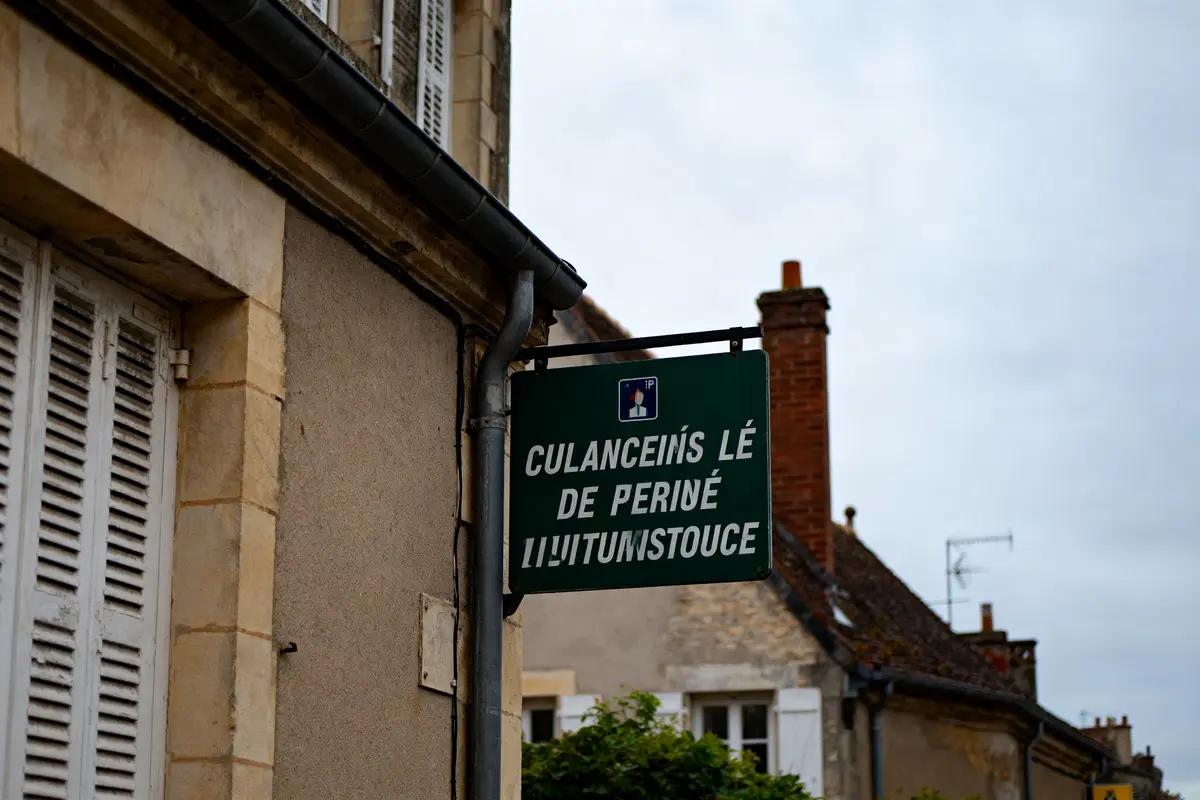 Panneau en langue gaélique sur un mur en pierre, immeubles anciens en arrière-plan.