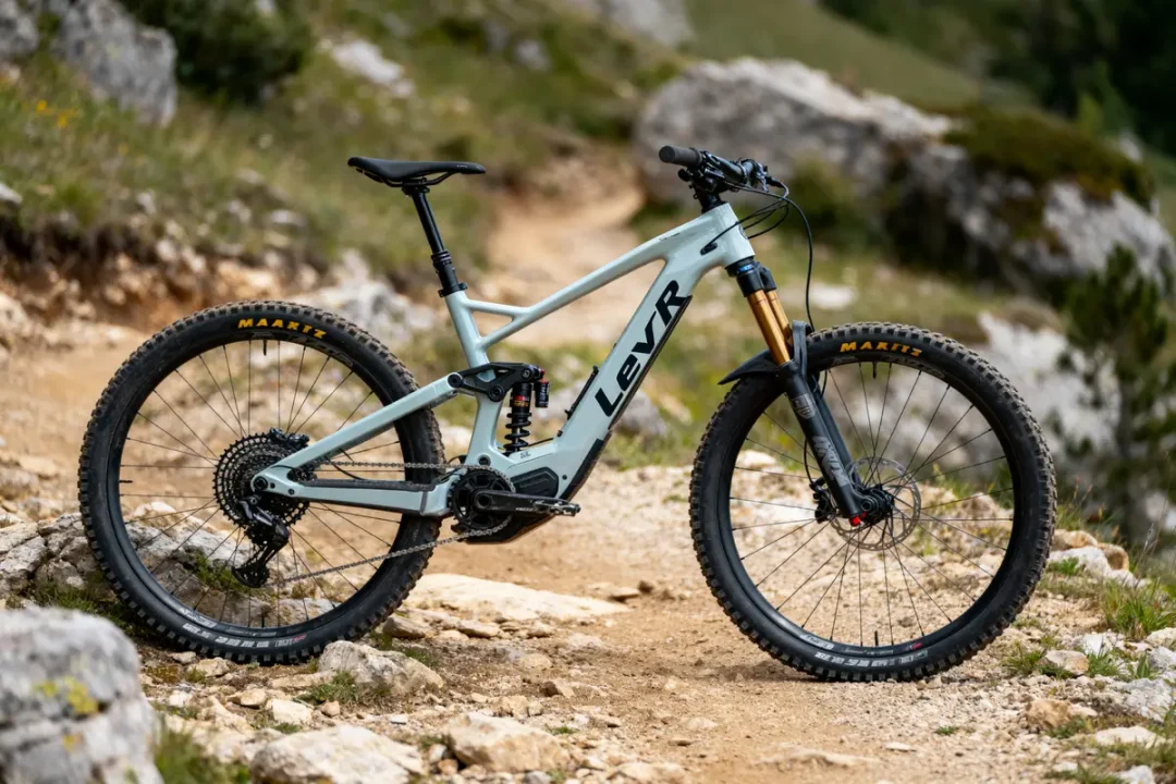 Vélo tout-terrain électrique gris sur chemin de montagne rocailleux, cadre Levr, pneus Maxxis. Environnement naturel.