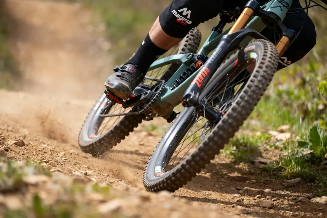 VTT descente sur sentier poussiéreux, vue rapprochée roues et pédales. Cycliste en équipements spécialisés.