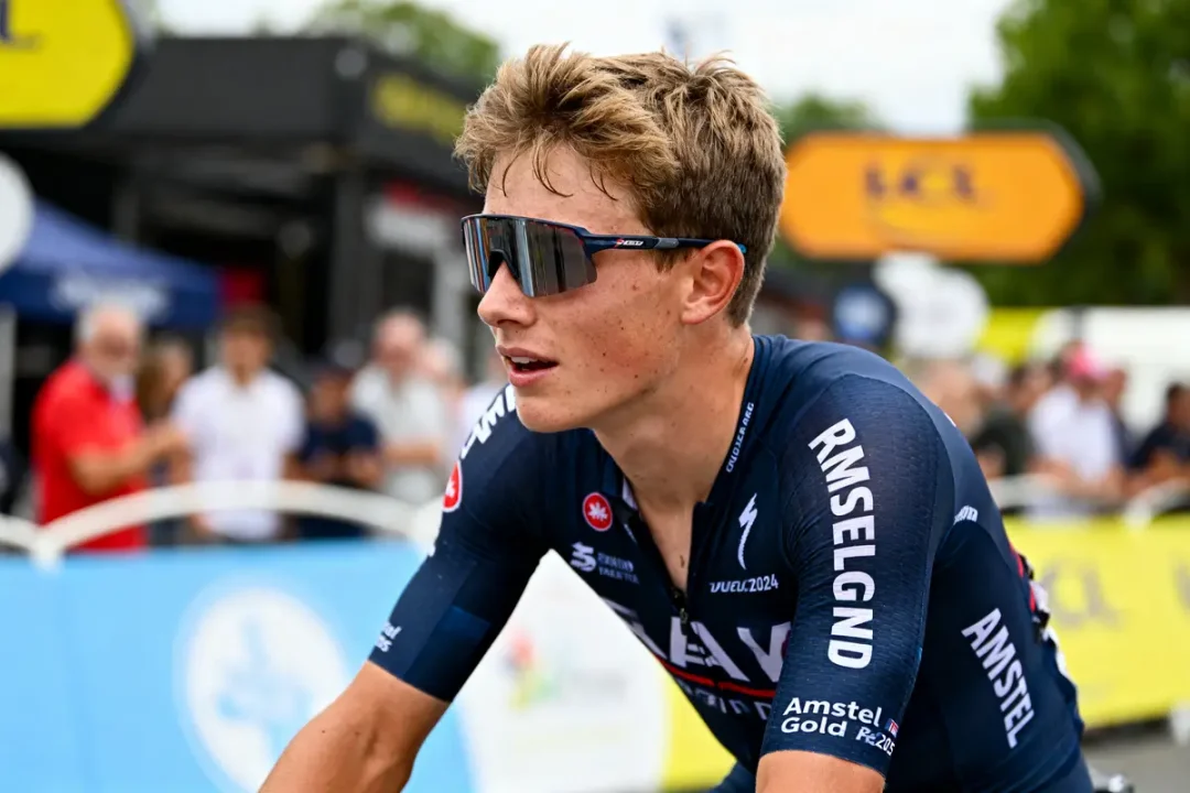 Cycliste en maillot bleu foncé, portant des lunettes de soleil, entouré de spectateurs flous lors d'un événement.