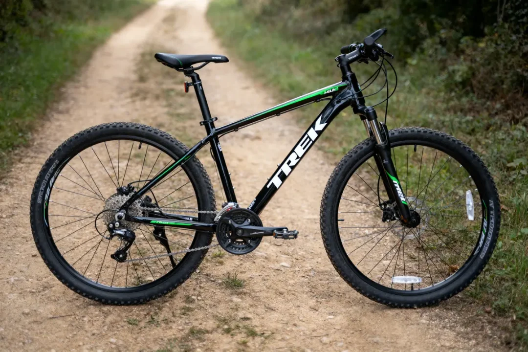 VTT noir et vert sur chemin de terre entouré de végétation.