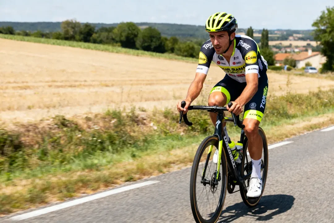 Un cycliste en tenue de course roule sur une route de campagne ensoleillée.