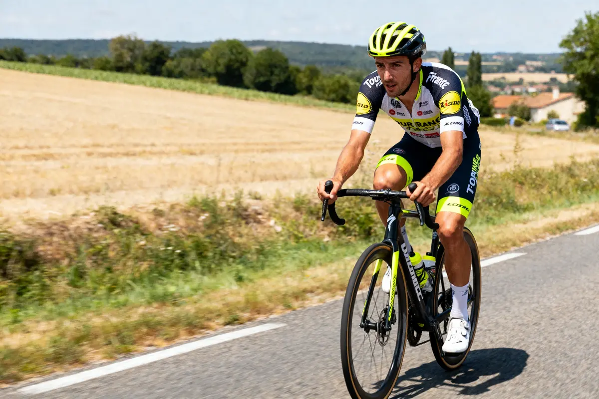 Un cycliste en tenue de course roule sur une route de campagne ensoleillée.