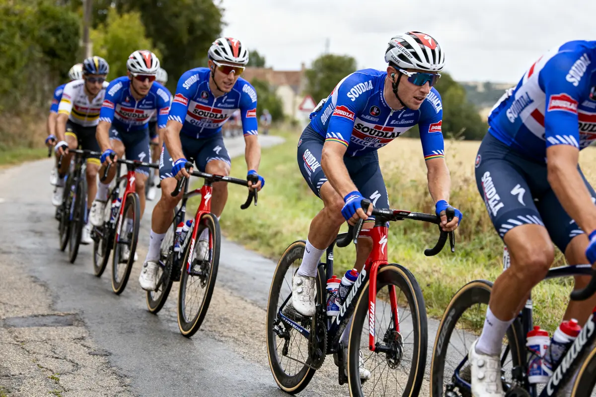 Cinq cyclistes en uniforme bleu, casques, en course sur une route de campagne.