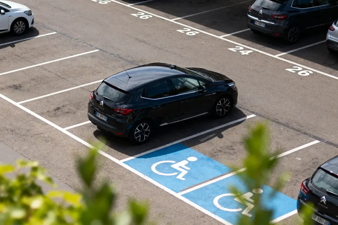 Voiture noire mal garée sur une place de parking pour personnes handicapées, marquage bleu visible.