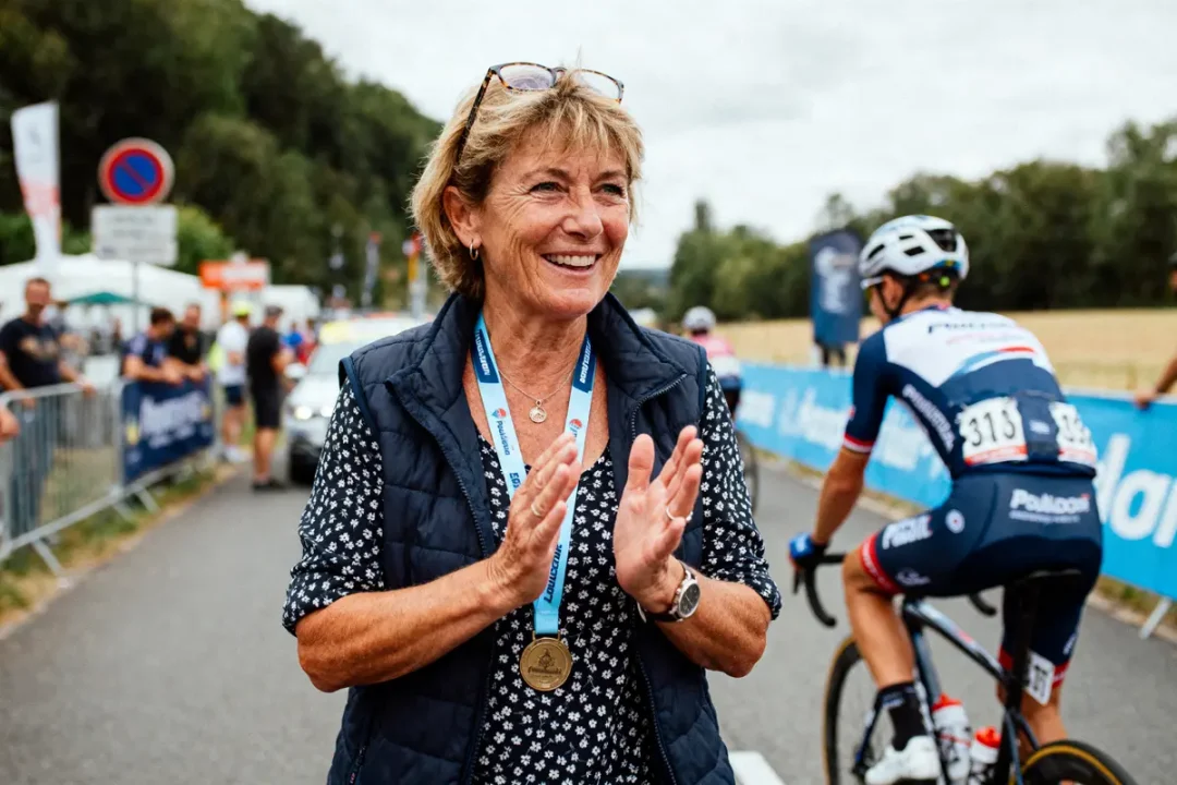 Femmes applaudissant, cycliste en compétition, route bordée de spectateurs, ambiance joyeuse et sportive, médaille au cou.
