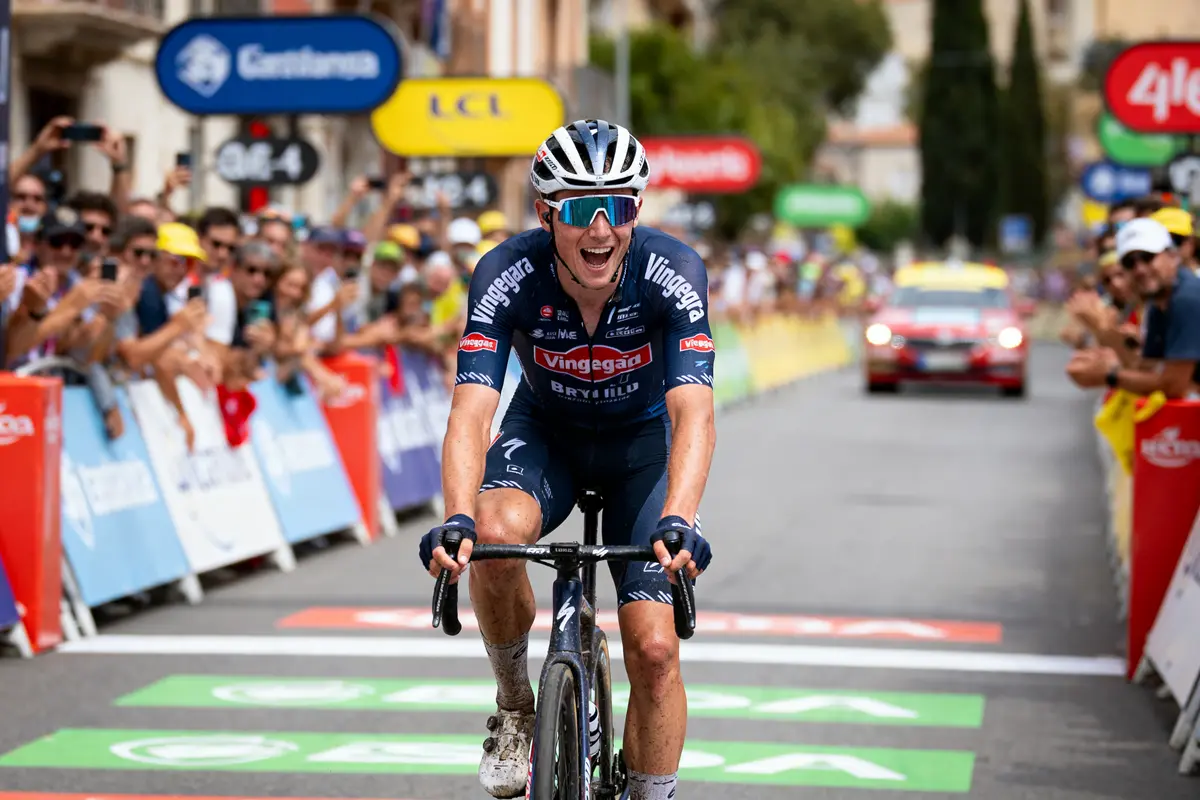 Cycliste franchissant la ligne d'arrivée en souriant lors d'une course, foule en arrière-plan applaudissant.