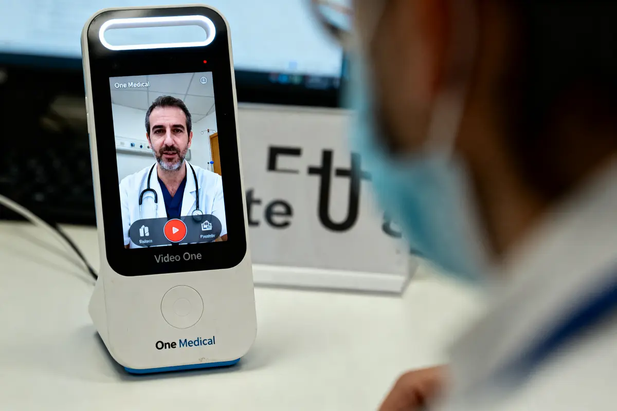 Appareil médical affichant un médecin en visioconférence, personne portant un masque en arrière-plan.