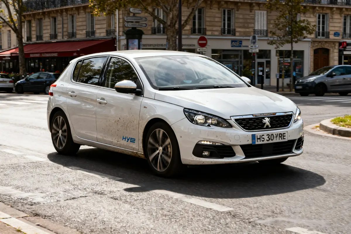 Voiture Peugeot 308 hybride blanche circulant en ville sur une route ensoleillée