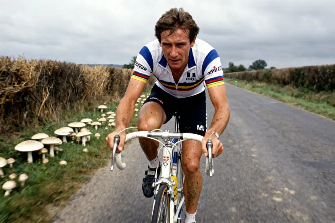Greg LeMond pédale en tenue de cycliste sur une route bordée de champignons blancs