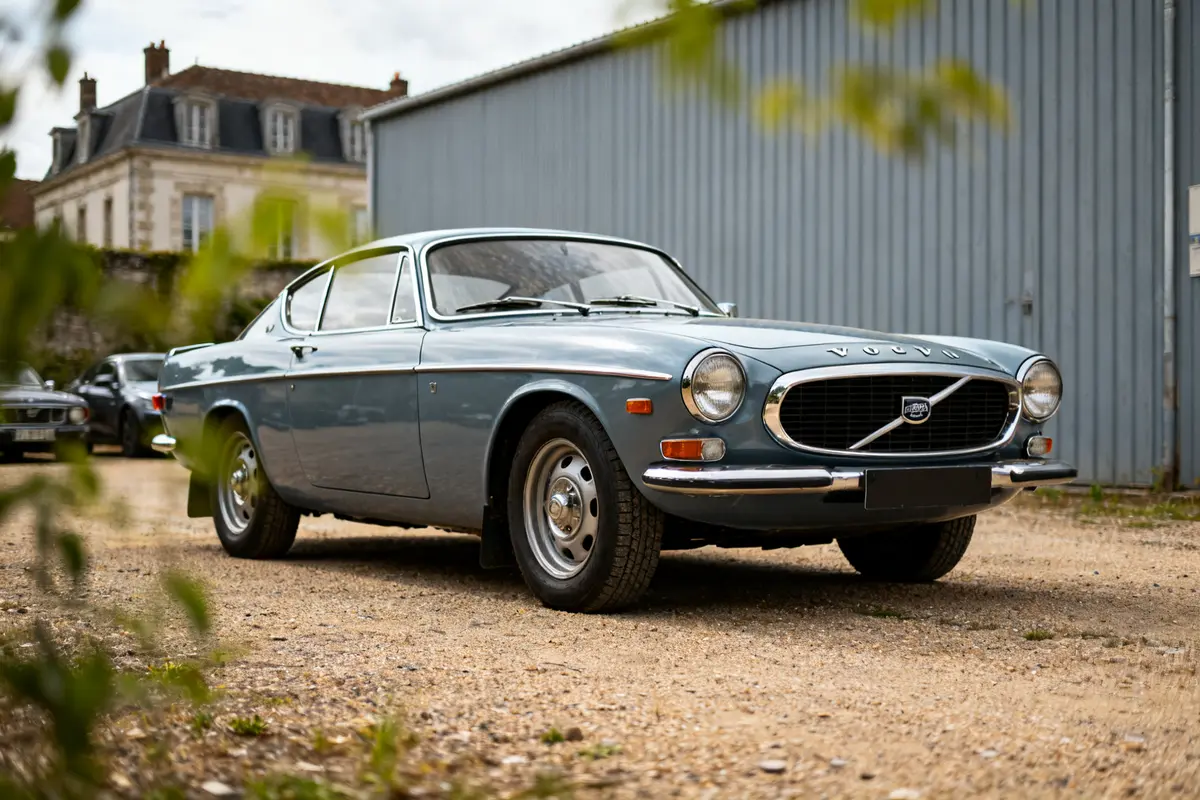 Voiture classique Volvo P 1800 stationnée devant un bâtiment en arrière-plan flou.
