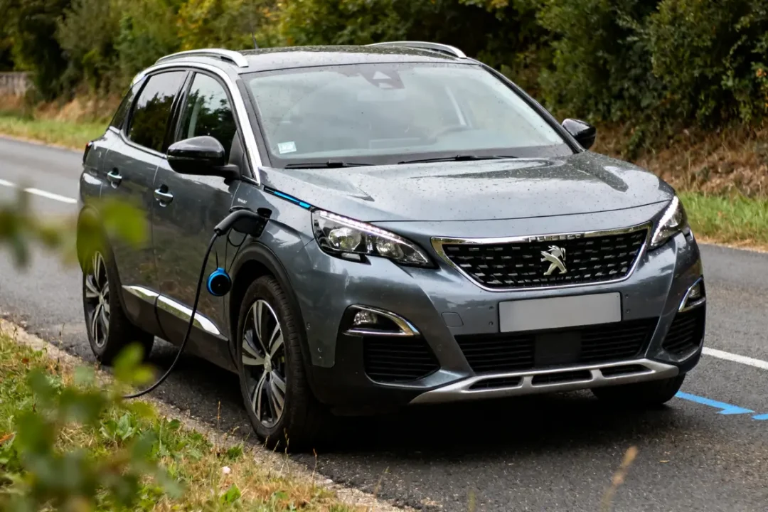 Hybride rechargeable Peugeot gris branché en recharge sur une route de campagne humide