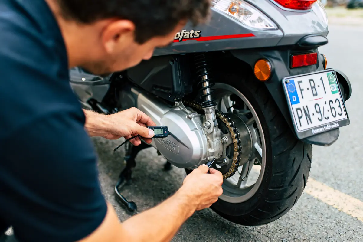 Homme vérifiant chaîne arrière d'un scooter scootfats avec un outil sur un parking