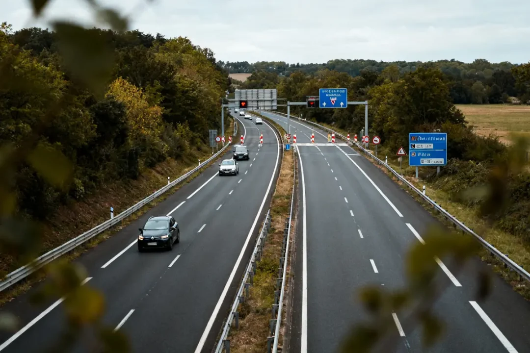 Voies rapide bordées d'arbres avec voitures et panneaux routiers visibles en arrière-plan