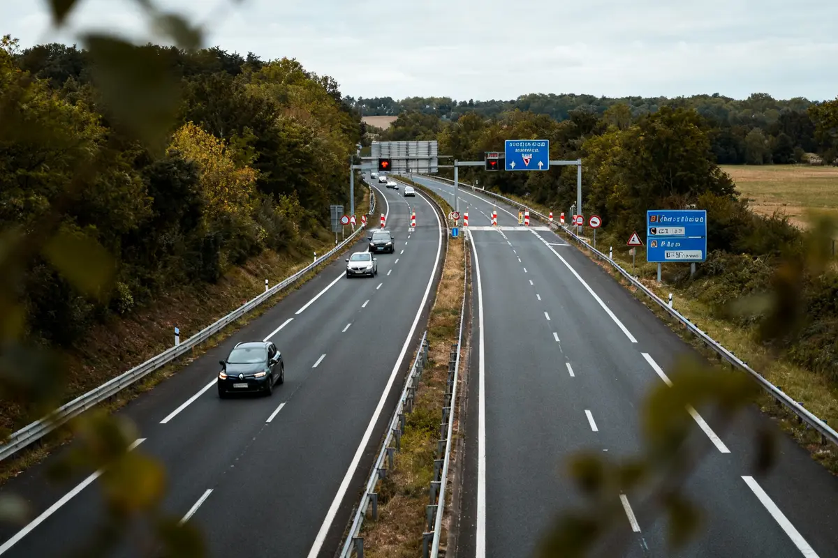 Voies rapide bordées d'arbres avec voitures et panneaux routiers visibles en arrière-plan