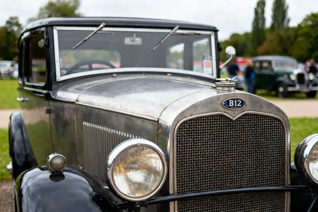 Voiture B12 rétro, avant grillagé, phares ronds, parc en arrière-plan, jour clair