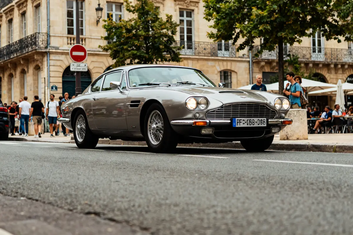 Voiture grac classique argentée sur une rue urbaine animée avec des passants et arbres