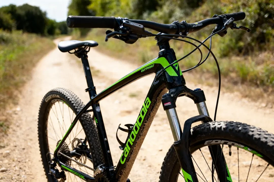 VTT Cannondale Super X vert et noir sur chemin terreux en forêt.