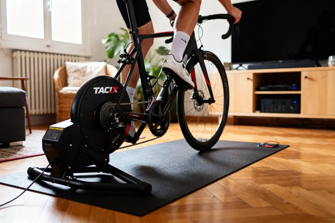 Cycliste à domicile utilisant le home trainer Tacx Flux S sur tapis noir